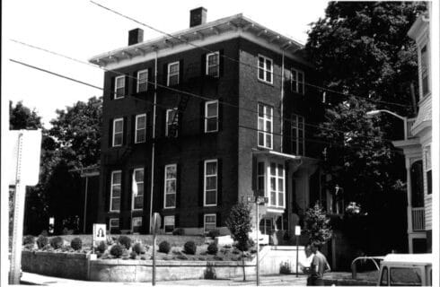 Black and white vintage photo of a large 3-story brick building on a city corner street.