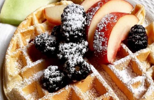 Belgian waffle topped with cherries and plum slices and dusted with powdered sugar.