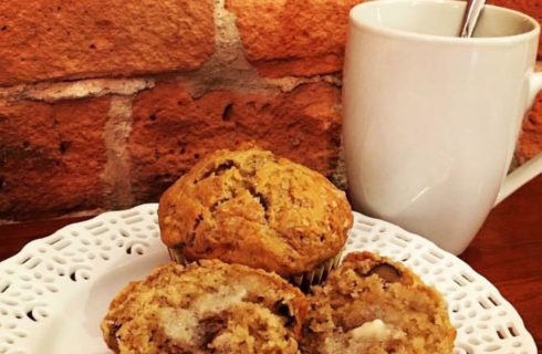 Three fresh muffins on a white plate accompanied by a hot beverage.