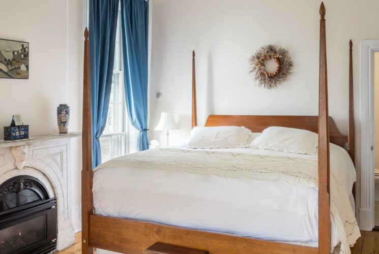 Large king four-post bed next to fireplace and large window.