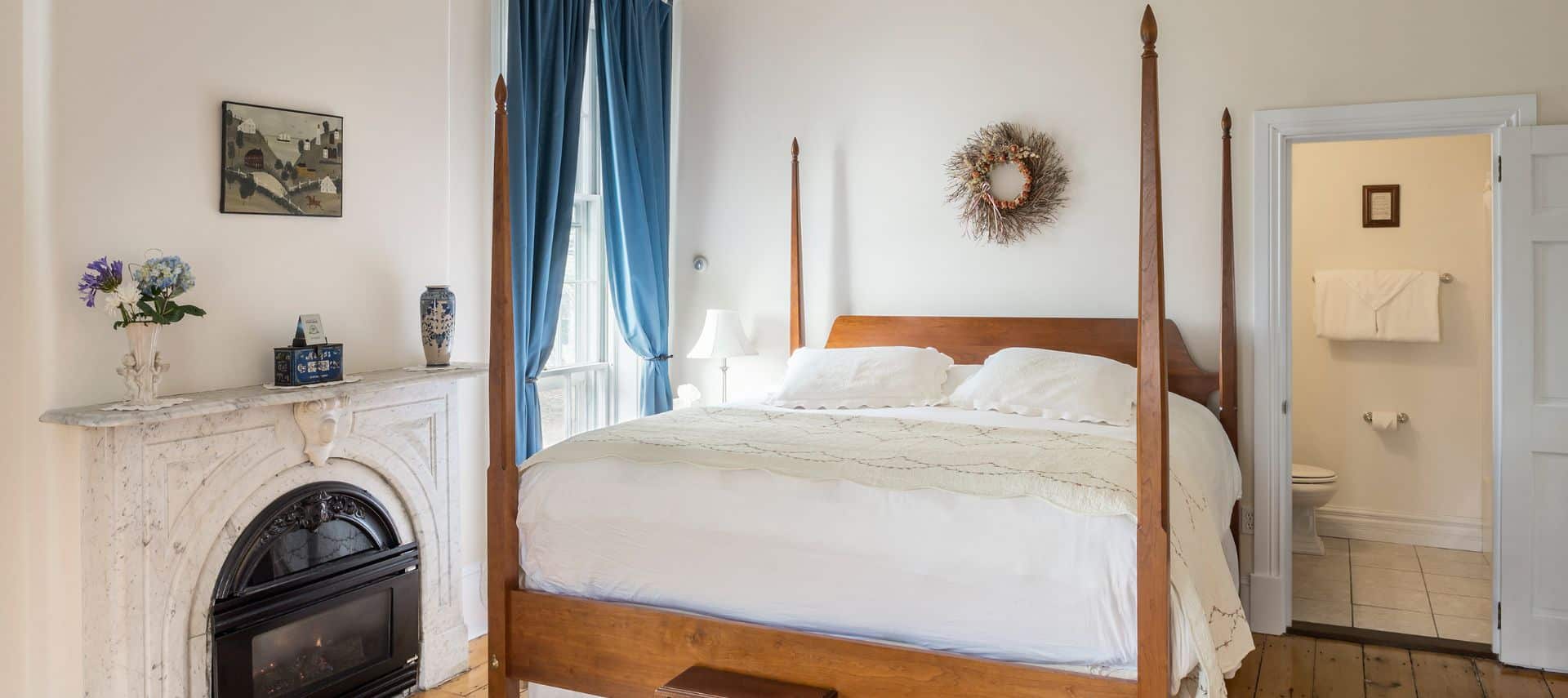 Large king four-post bed next to fireplace and large window.