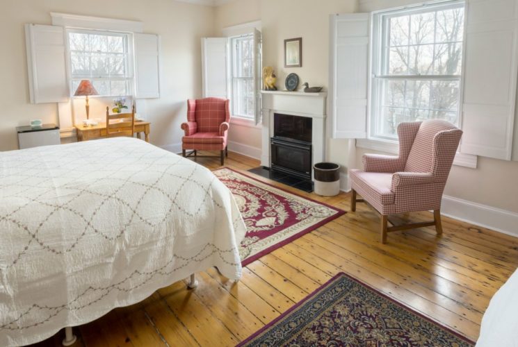 King and twin beds in a spacious bedroom with a wooden armoire and red wing back chairs.