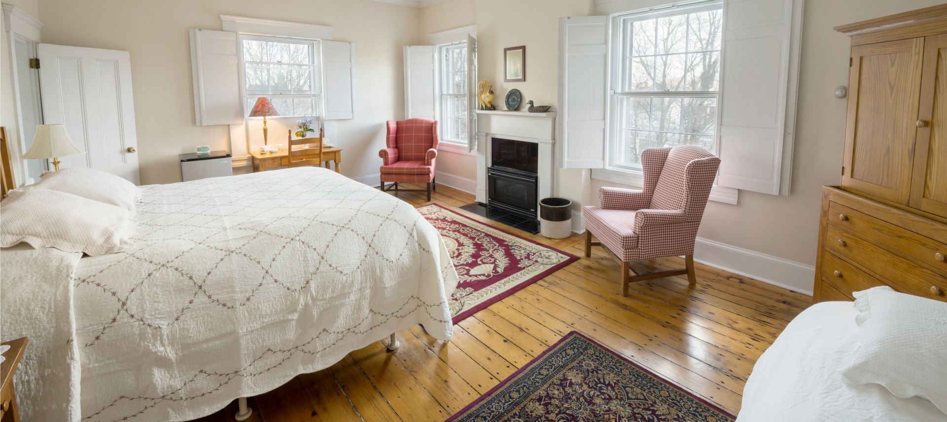 King and twin beds in a spacious bedroom with a wooden armoire and red wing back chairs.