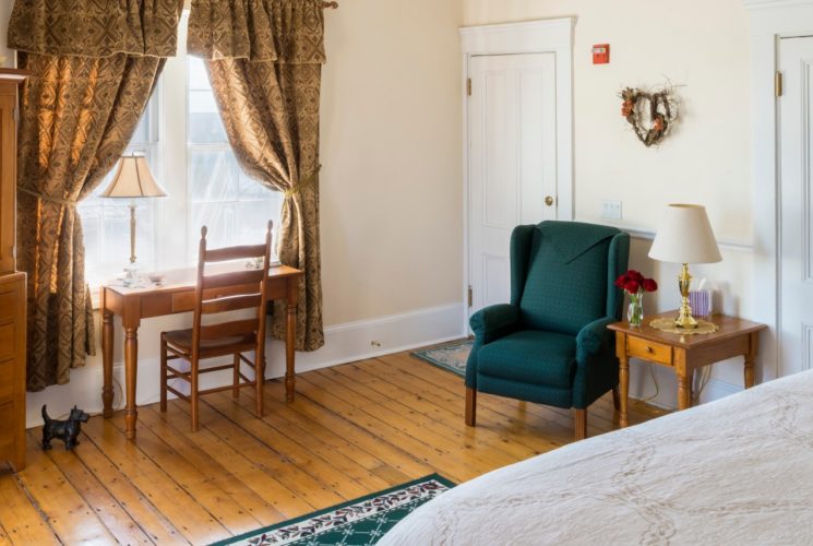 Big bright bedroom with large windows, a wooden armoire and a desk.