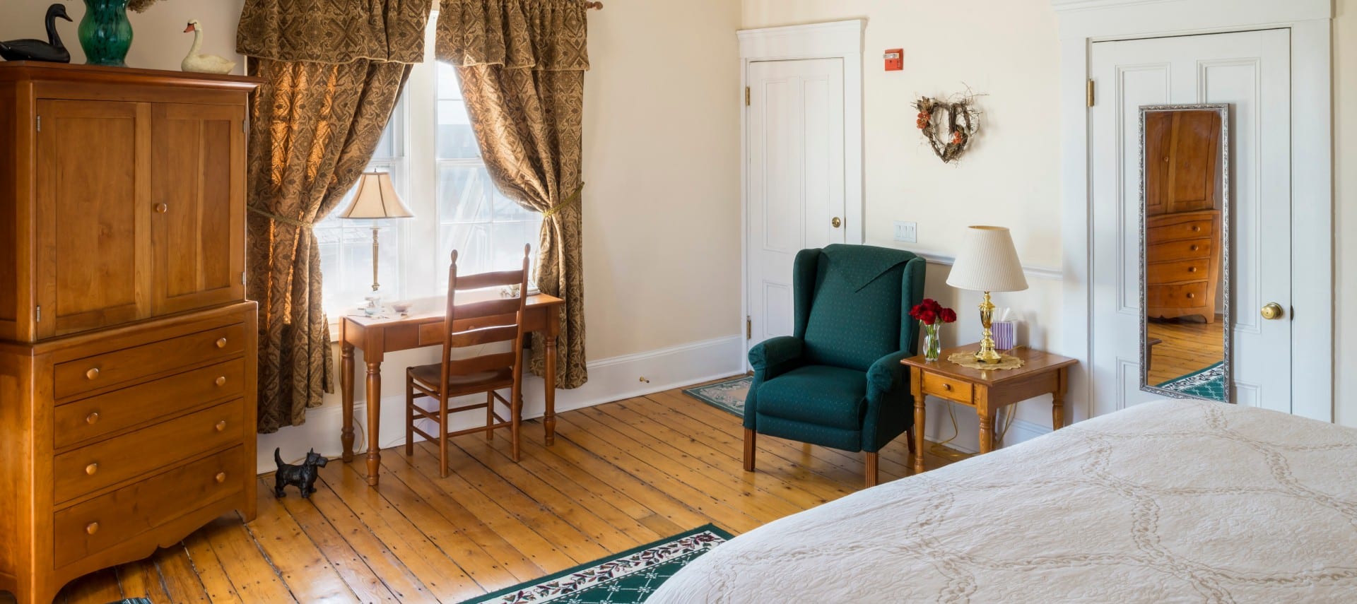 Big bright bedroom with large windows, a wooden armoire and a desk.