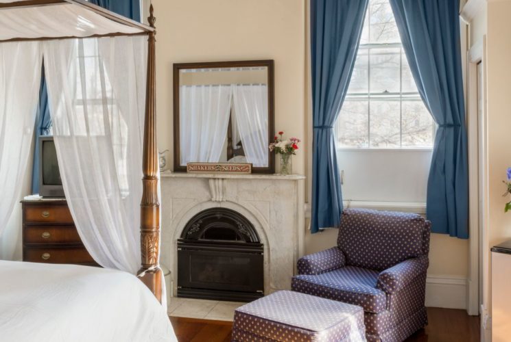 Queen canopy bed faces a marble fireplace with a mirror over it and a dresser with a TV.