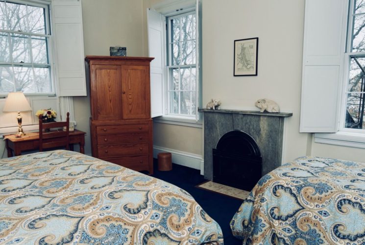 Bedroom with a twin and king bed, a fireplace, a window and a wooden armoire and desk.