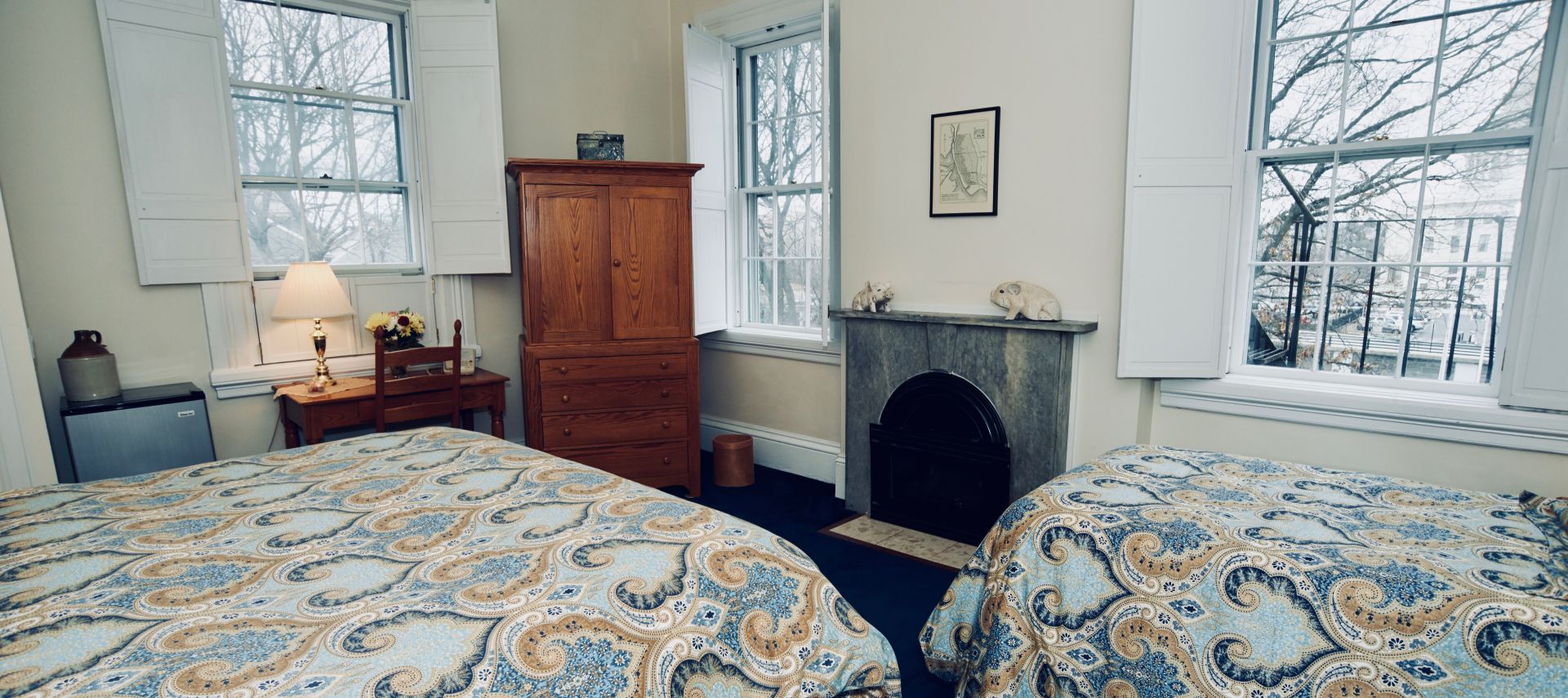 Bedroom with a twin and king bed, a fireplace, a window and a wooden armoire and desk.