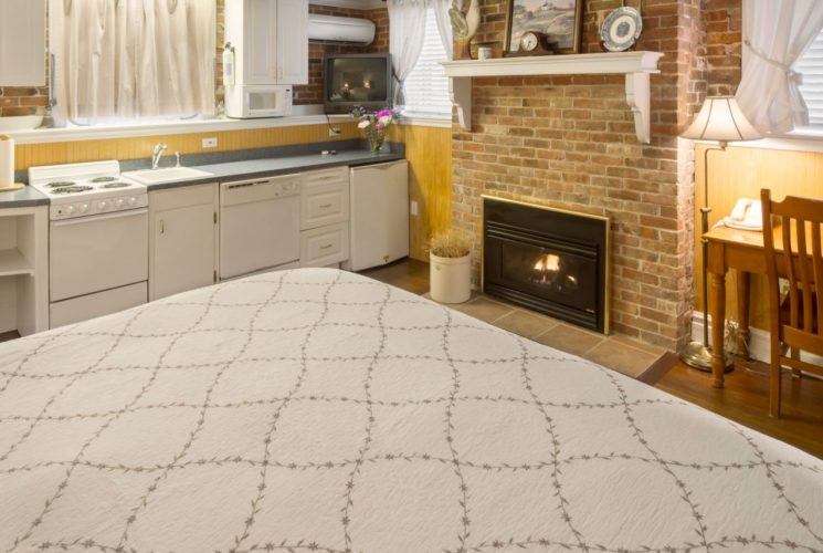 A king bedroom featuring a kitchenette, brick fireplace, and a wooden desk.
