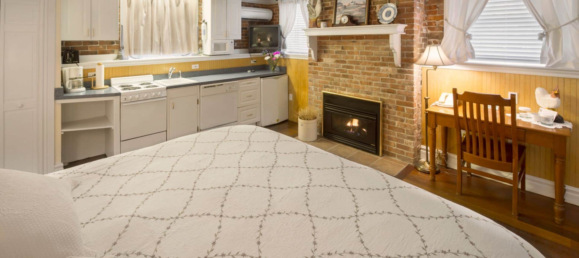 A king bedroom featuring a kitchenette, brick fireplace, and a wooden desk.