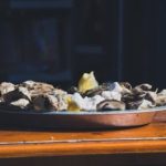 Shucked oysters on a silver plater with a slice of lemon.