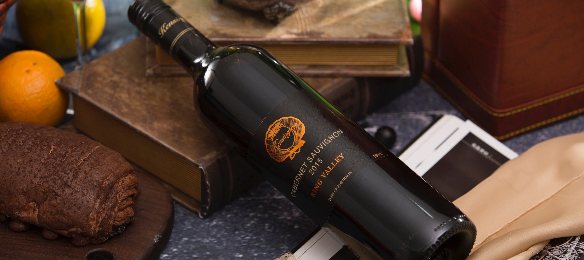 A dark bottle of wine propped up on books next to wine glasses.