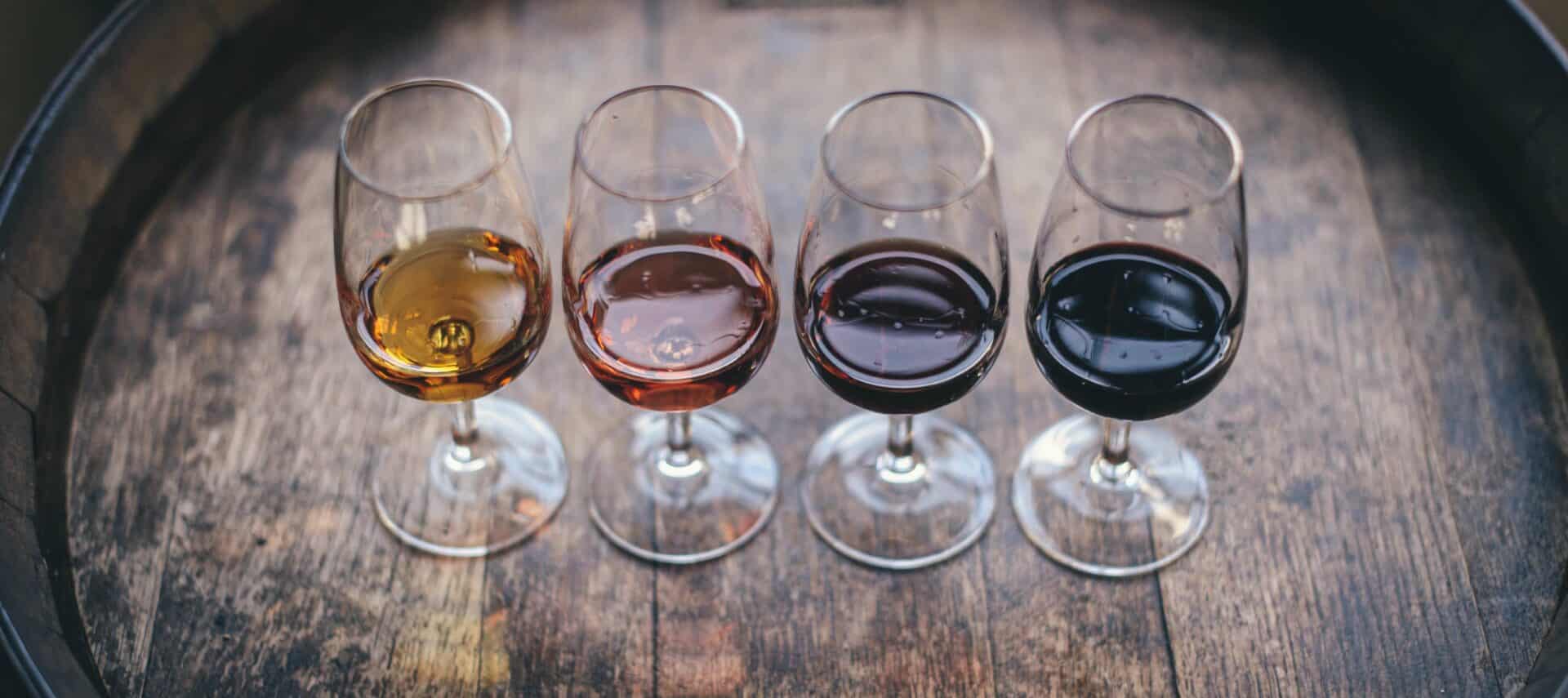 Four stemmed wine glassed filled with various flavors ontop of a wine barrel.